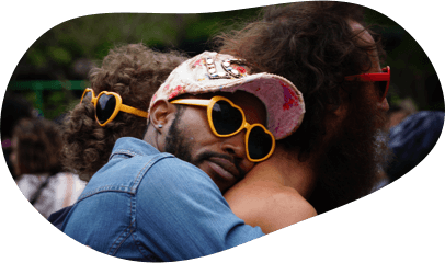 A Black man, wearing yellow heart-shaped sunglasses, hugs another man’s back