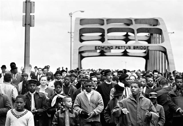 Hundreds of Black marchers cross the Edmund Pettus Bridge. A few children are visible at the front of the march.
