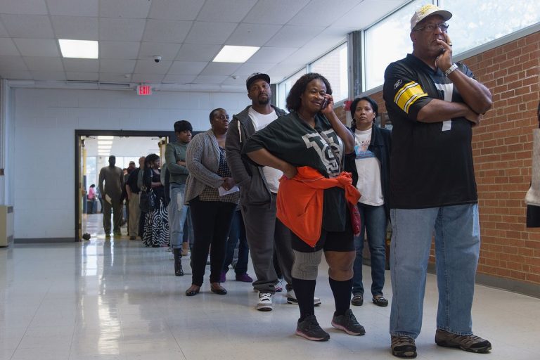 A contemporary photo shows Black voters lined up in the corridor and doorframe of a hallway.