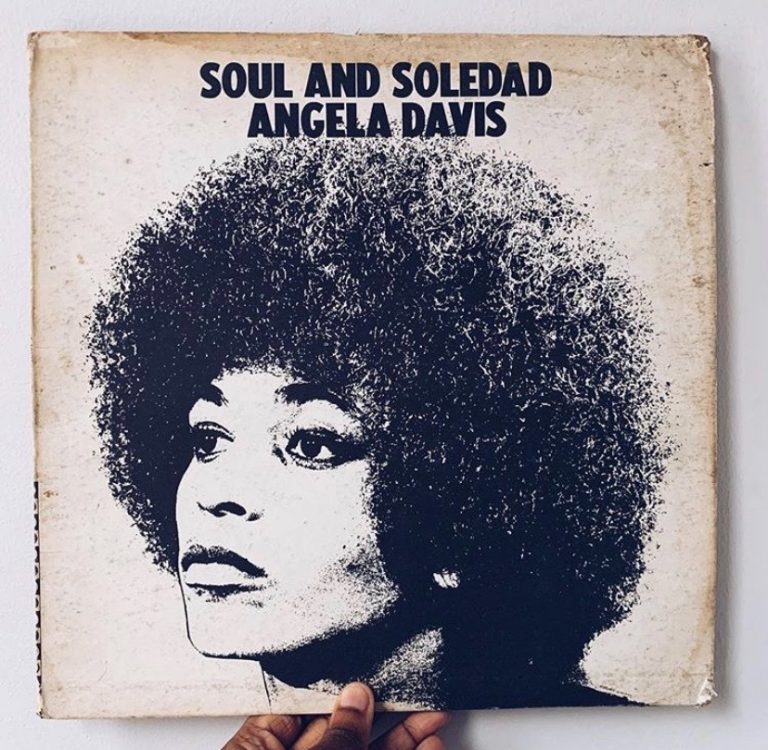 A hand holds a vintage record with a graphic photo of Angela Davis and text that reads "SOUL AND SOLEDAD ANGELA DAVIS"