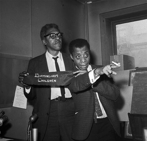 Bayard Rustin and James Baldwin hold a cloth sign that reads "Birmingham Children". Baldwin points his right hand, with cigarette, off to the right of the photo frame.