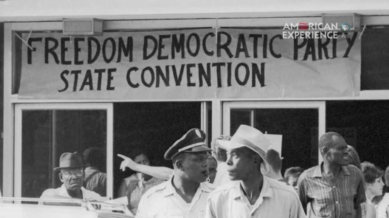 A cluster of people look in different directions below a banner that reads "Freedom Democratic Party State Convention"